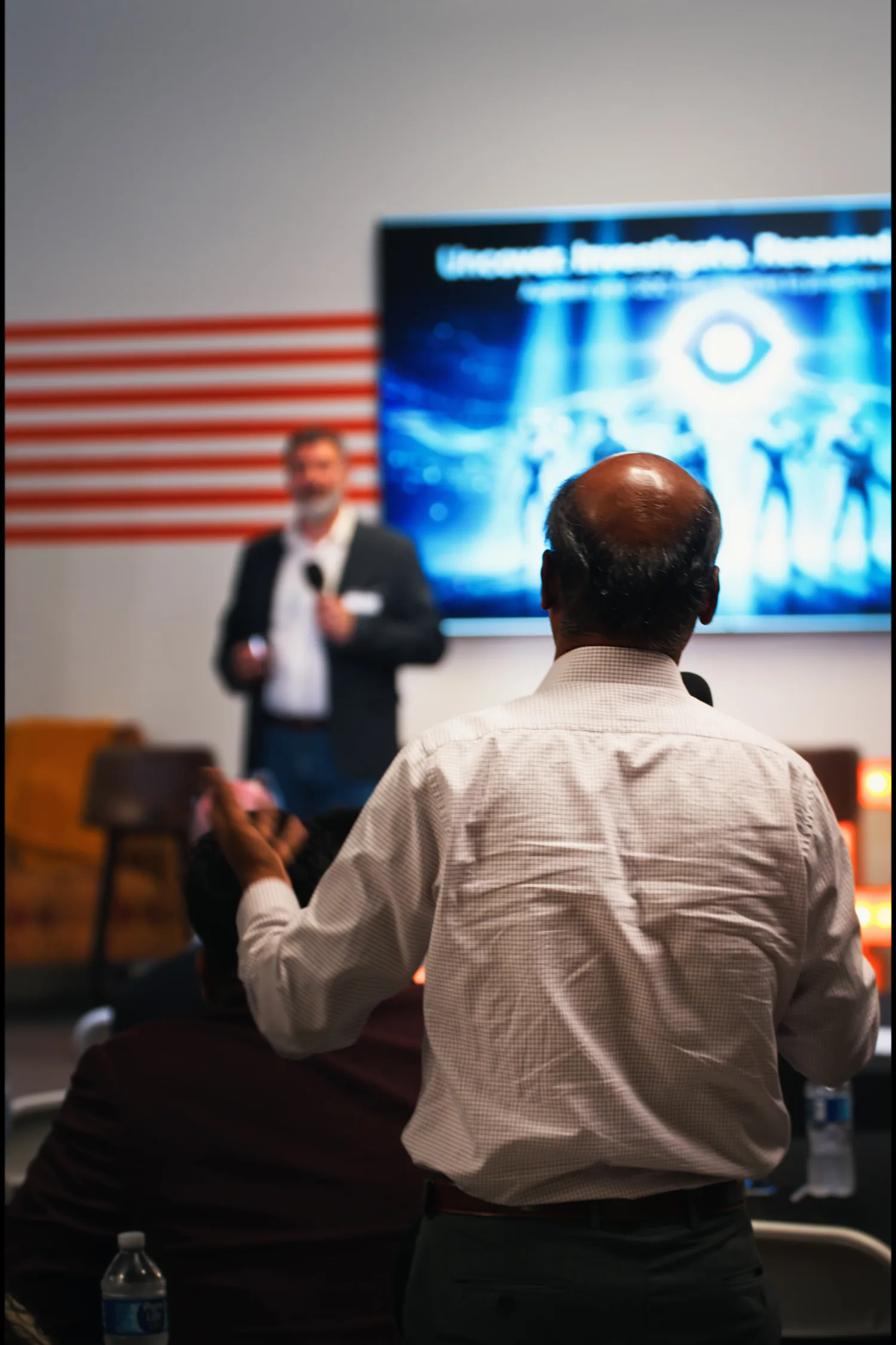 An attendee standing to ask a question during the forum, the speaker in the background.